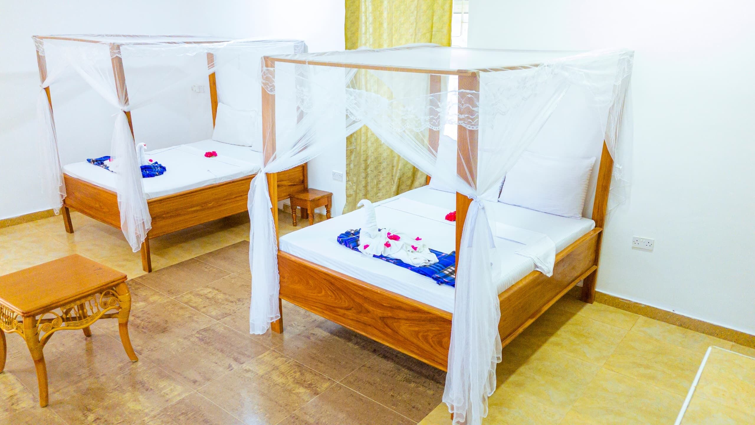Two wooden beds with white canopies, a small wooden table, and a tiled floor.