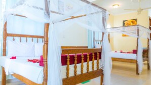 A room with two wooden four-poster beds, each covered with white sheets and red pillows. - Sands inn Hotel (Pwani Mchangani)