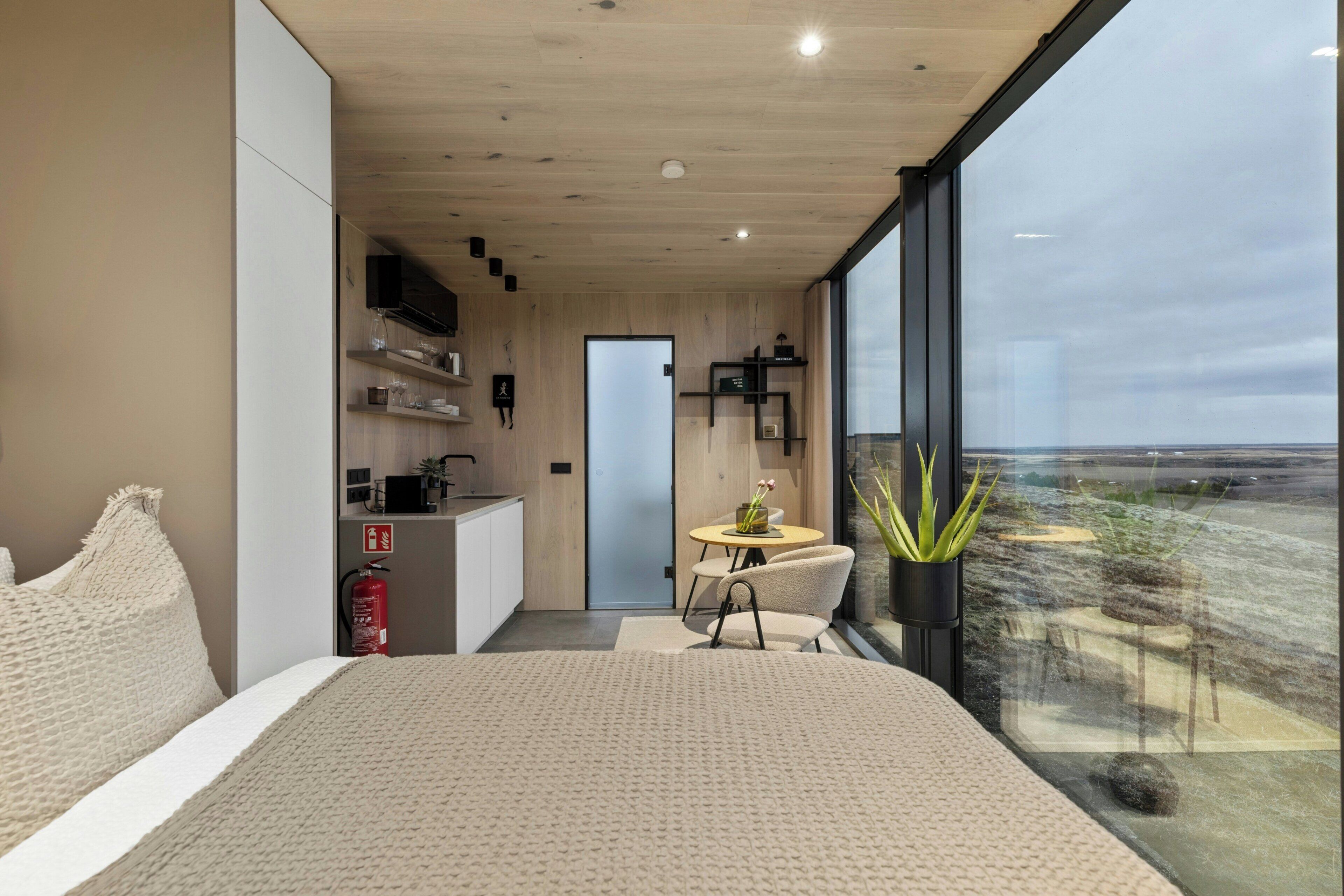 A modern bedroom with a large bed, a small dining area, and a view of the landscape.