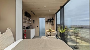 A modern bedroom with a large bed, a small dining area, and a view of the landscape.