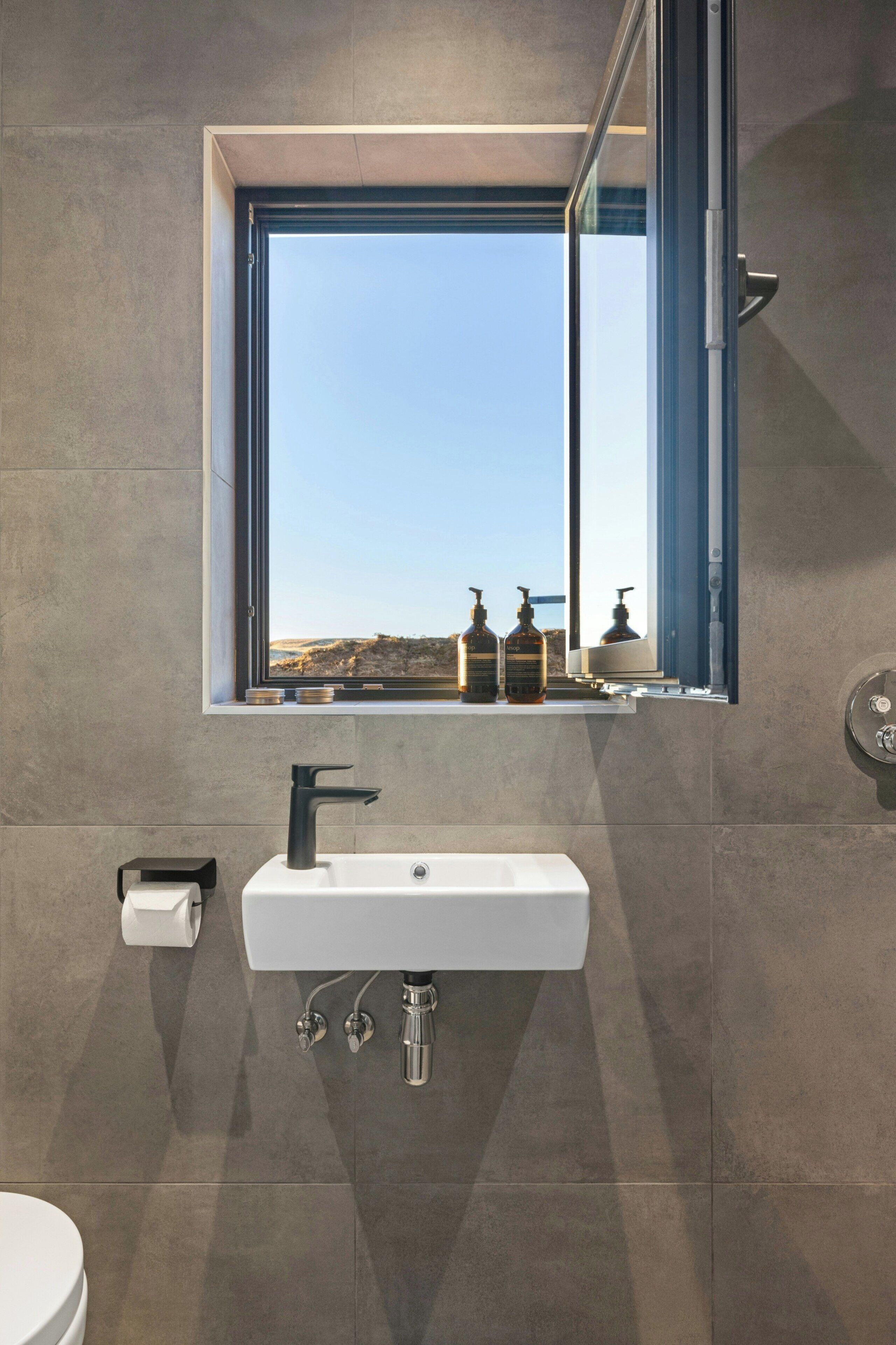 Une salle de bain moderne avec une grande fenêtre, un lavabo blanc et des toilettes.