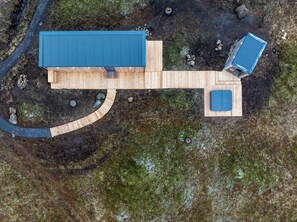 An aerial view of a wooden cabin with a blue roof, a circular wooden deck, and a small blue structure. - ÖÖD Hekla Horizon (Rangárþing ytra)