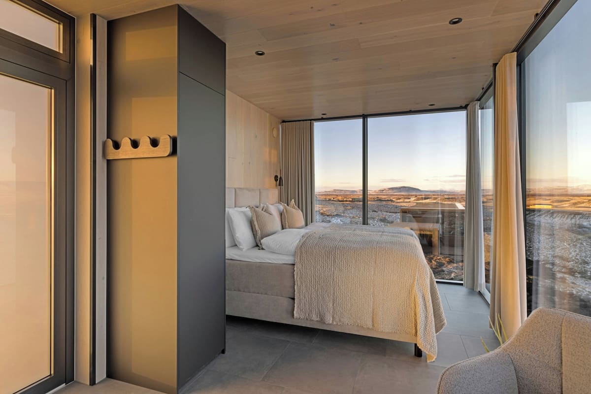A modern bedroom with a large bed, a bedside table, and a view of a mountainous landscape.