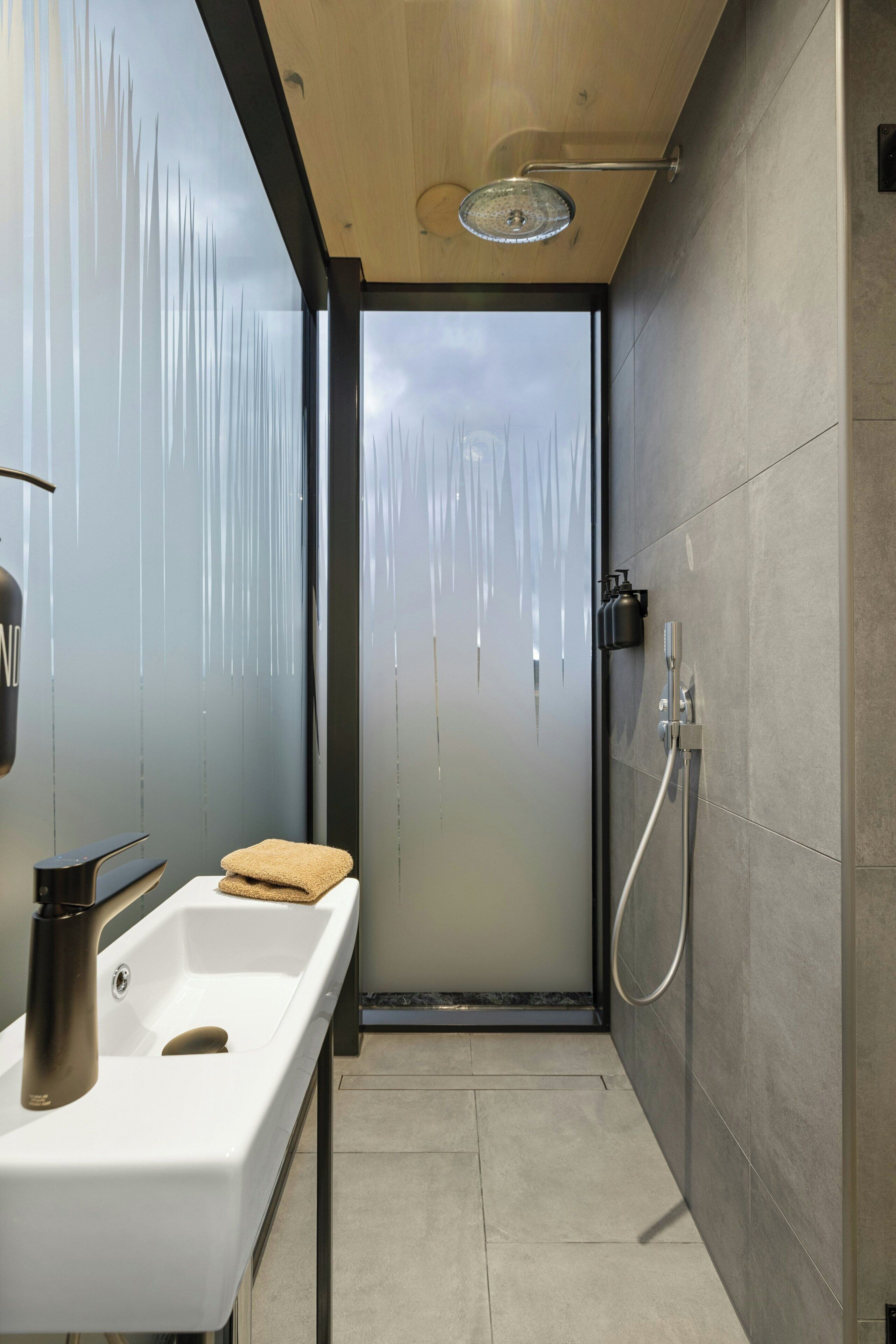 A modern bathroom with a glass shower door, a white sink, and a towel.