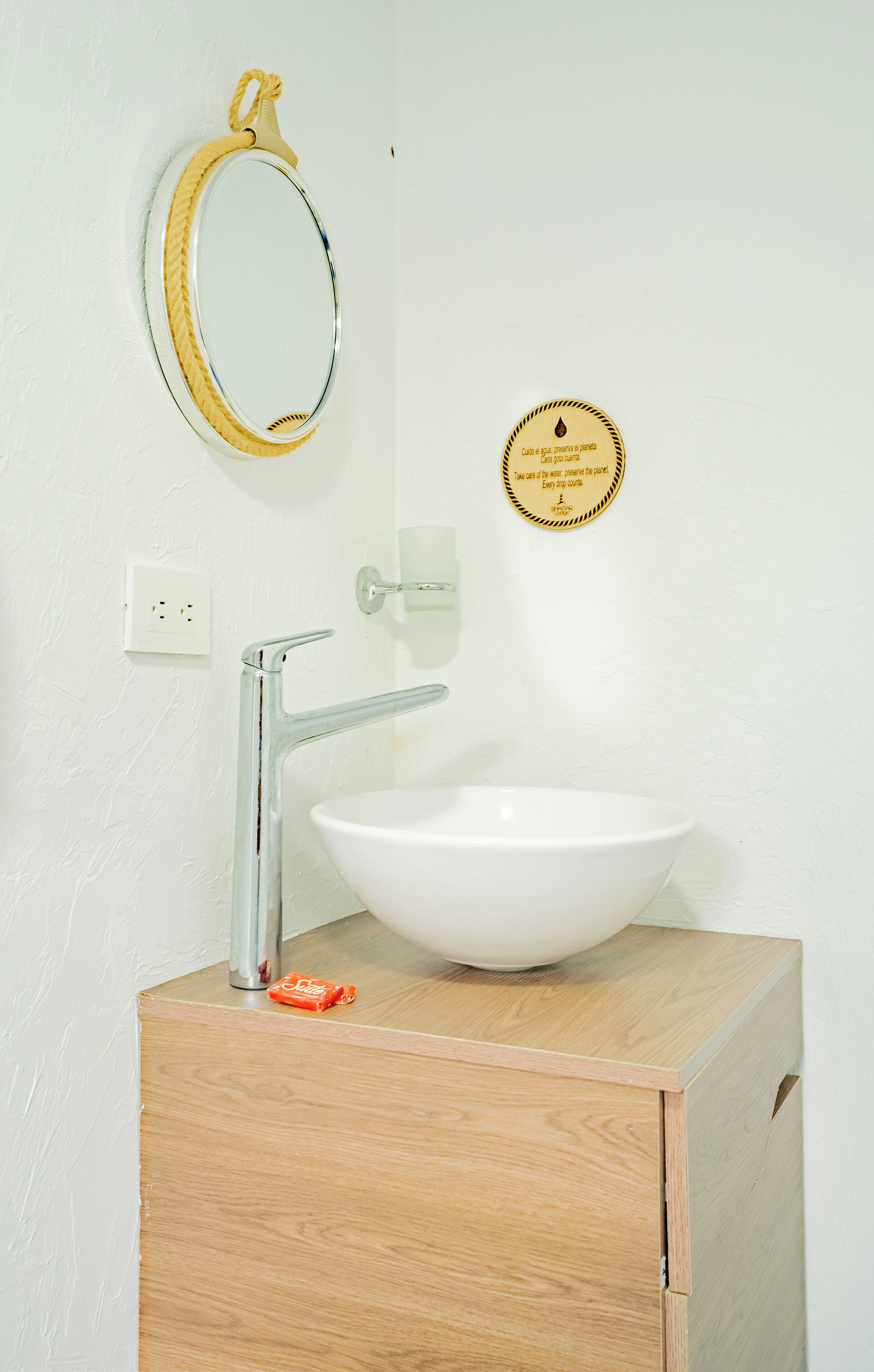Une salle de bain avec un lavabo blanc, un miroir et un distributeur de savon posé sur un meuble en bois.