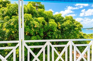 Un balcone bianco con vista su alberi verdi e un cielo azzurro.