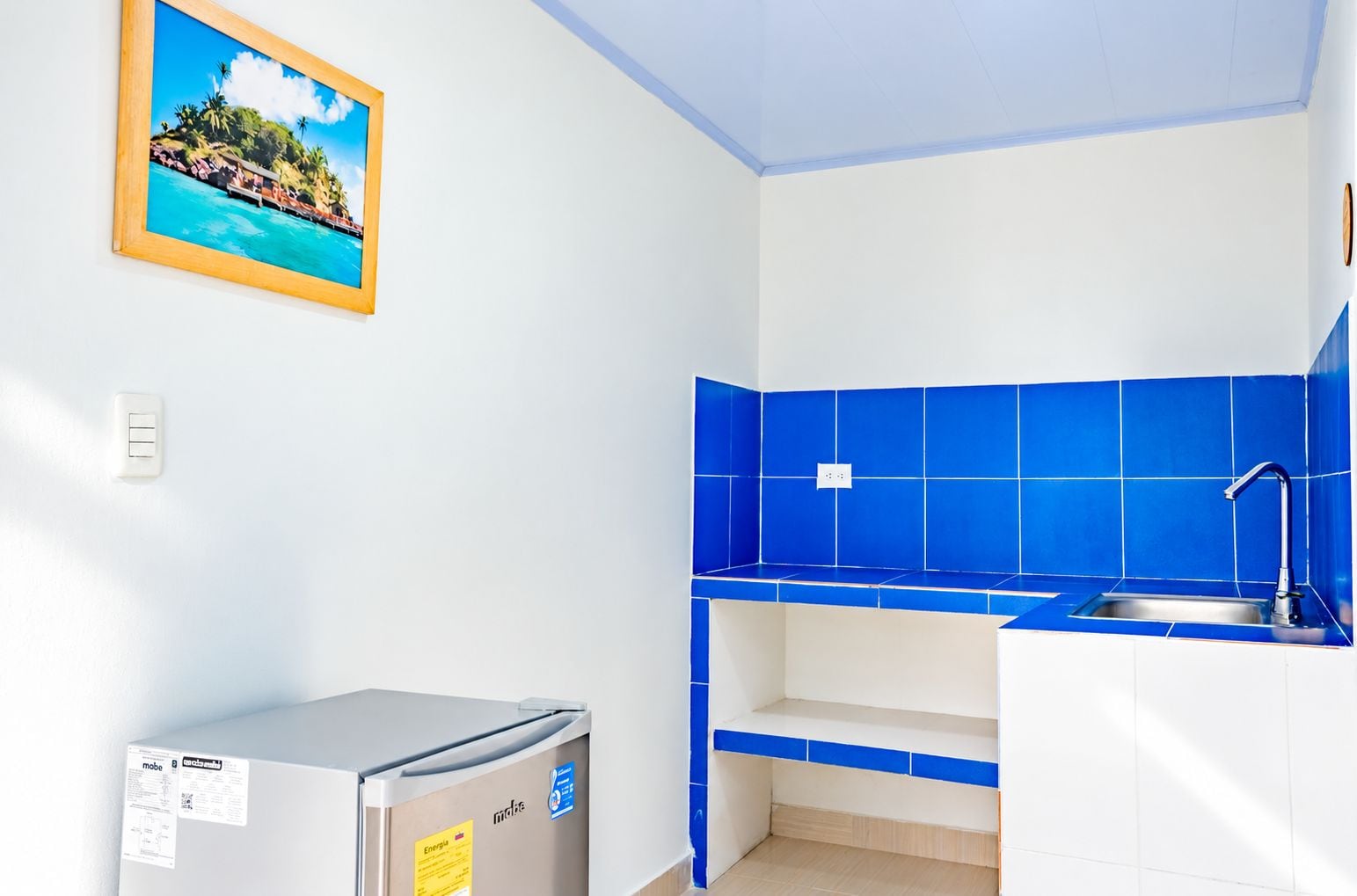 A compact kitchen with blue tiles, a small refrigerator, and a sink.