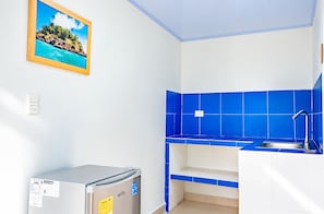 A compact kitchen with blue tiles, a small refrigerator, and a sink.