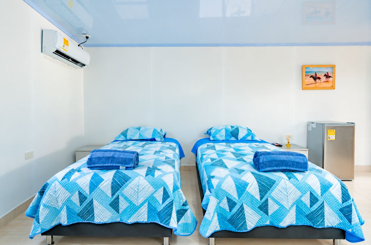 A hotel room with two beds, a small refrigerator, and a painting on the wall.