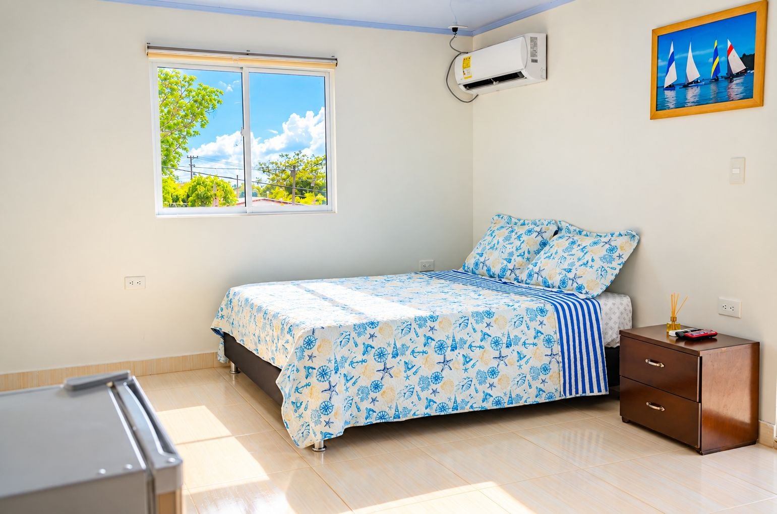 Un dormitorio con cama, mesita de noche, ventana y aire acondicionado.