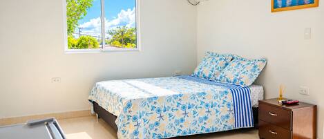 Un dormitorio con cama, mesita de noche, ventana y aire acondicionado.