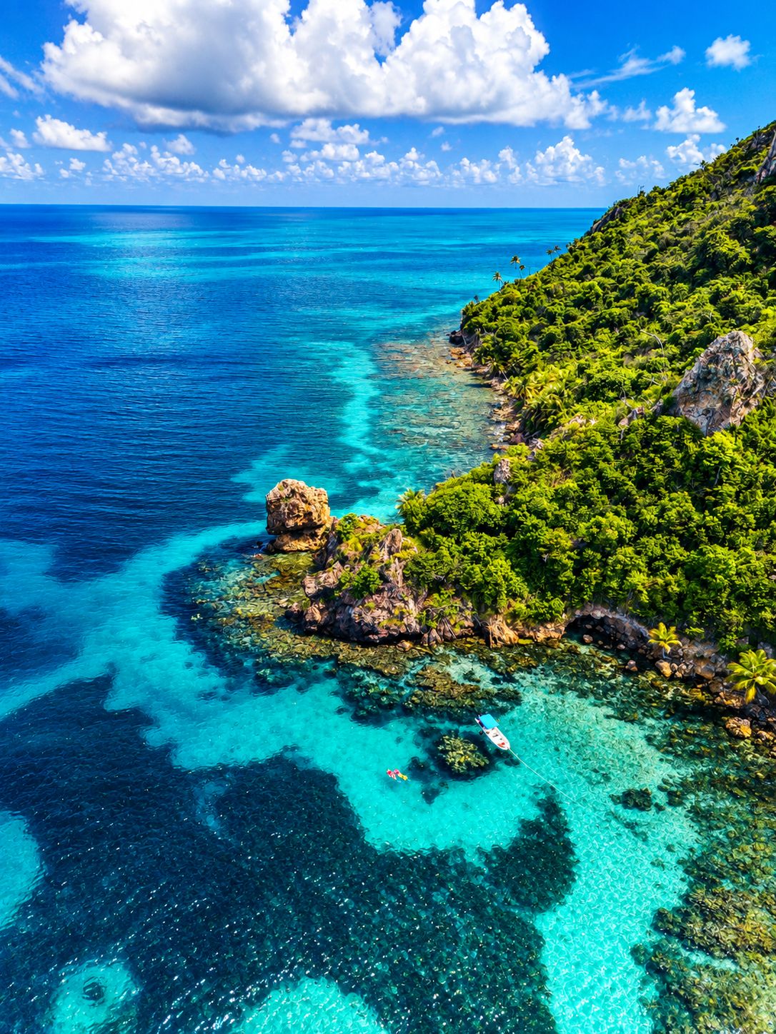 Eine Küstenlandschaft mit klarem türkisblauem Wasser, felsigen Landzungen und üppigem Grün.