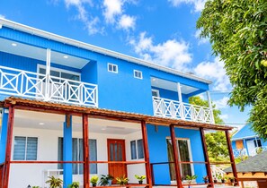A two-story building with a blue exterior, white balconies, and a covered porch area with potted plants. - SHAMAR LODGE  (Providencia)