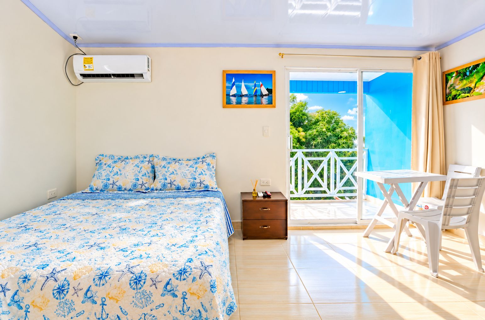 A bedroom with a bed, a nightstand, a table with chairs, and a balcony with a view.