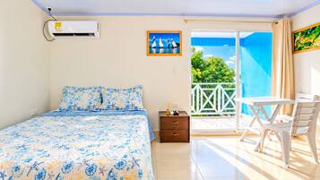 A bedroom with a bed, a nightstand, a table with chairs, and a balcony with a view.