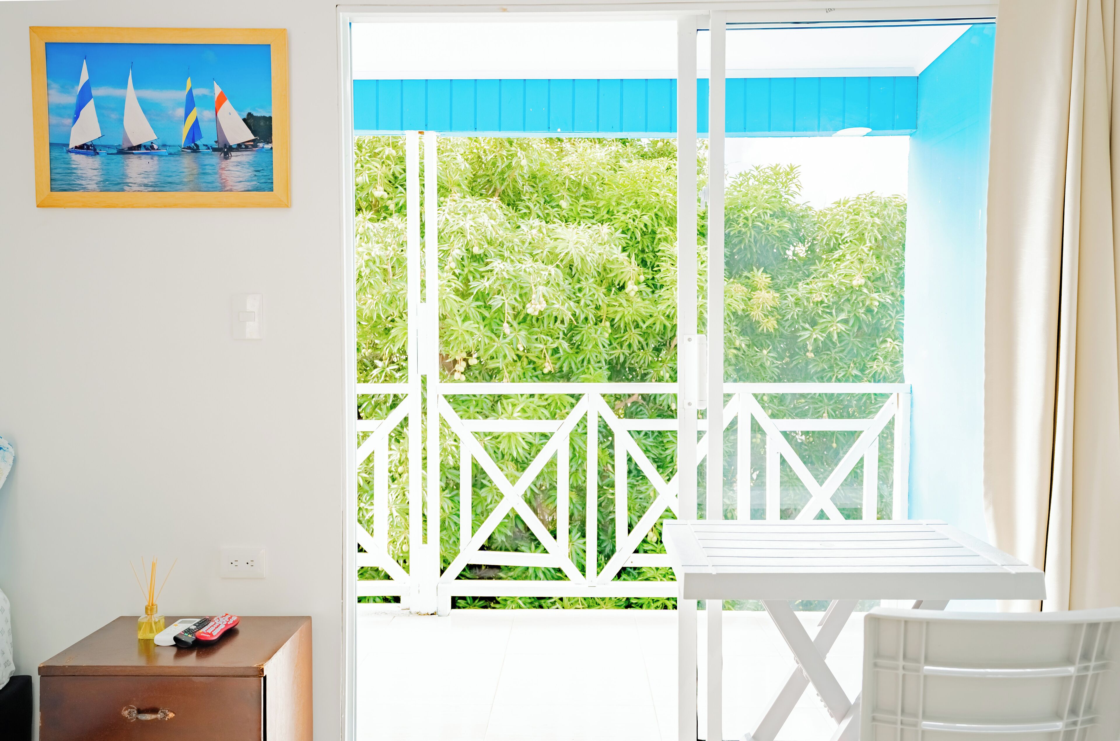 Habitación con balcón, una mesa, una silla, un archivador pequeño y un cuadro con barcos de vela.