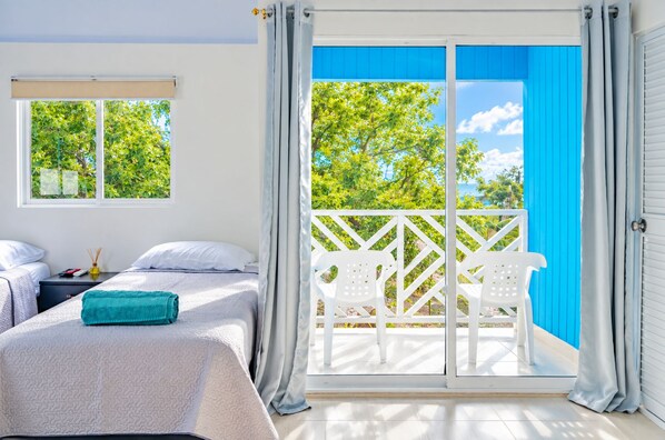 A bedroom with a bed, two white chairs, a window, and a balcony with a view of trees. - SHAMAR LODGE  (Providencia)