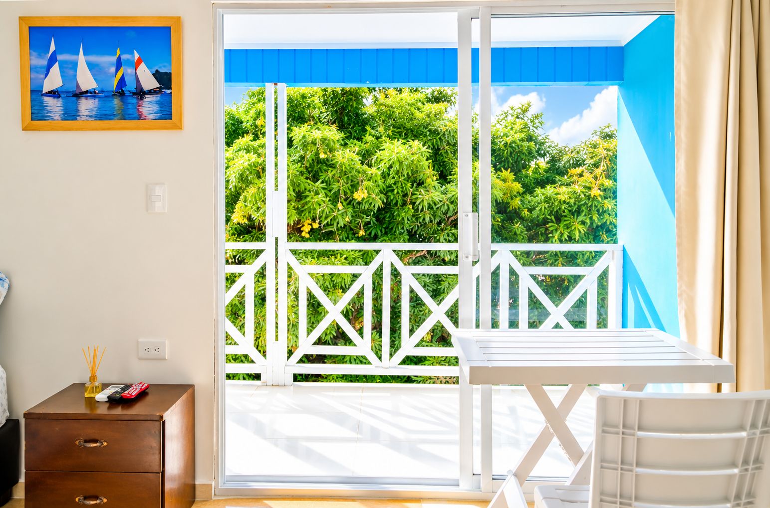 Une pièce dotée d’une porte-fenêtre coulissante qui donne sur un balcon avec une balustrade blanche et de la verdure à l’extérieur.