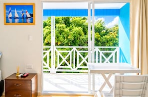 A room with a sliding glass door leading to a balcony with a white railing and greenery outside.