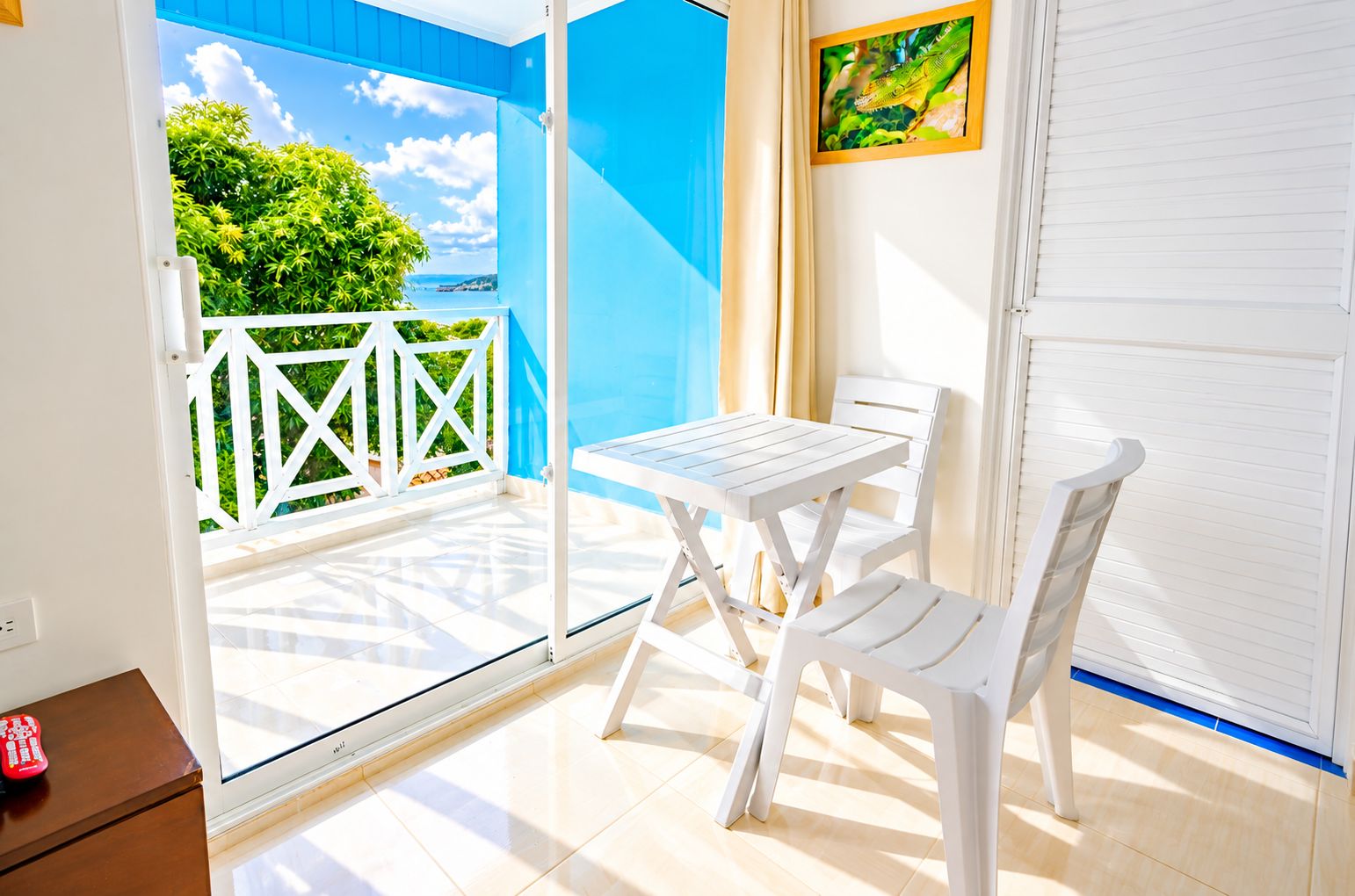 En balkon med et bord og stole, udsigt til grøn bevoksning og en blå himmel.