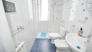A bathroom with a glass-enclosed shower, two toilets, a sink, and a blue mat on the floor.