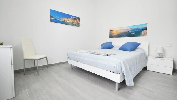 A modern bedroom with a bed, a chair, a nightstand, and two wall-mounted paintings.