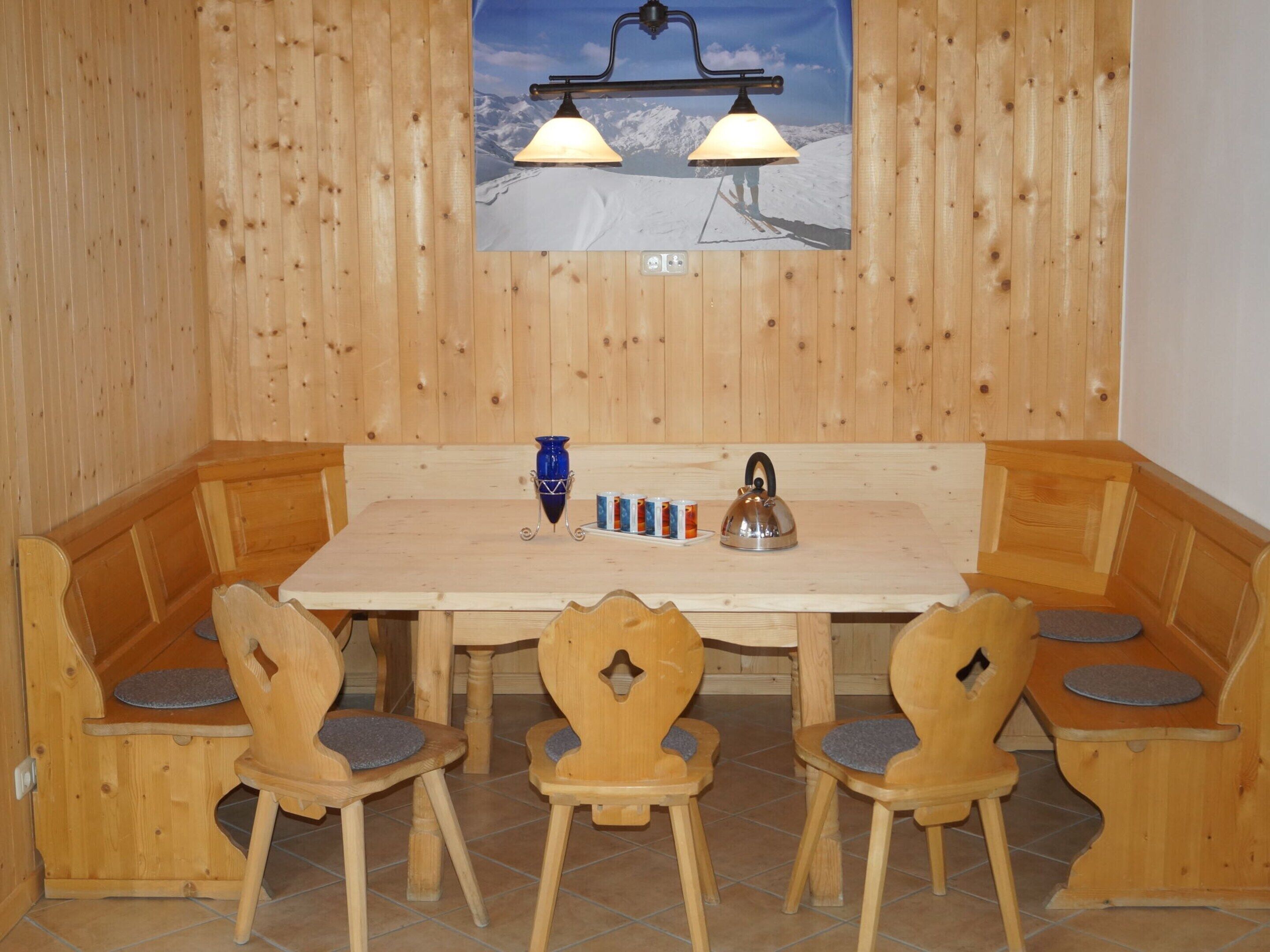 A wooden dining area with a table and benches, a blue vase, and a kettle.