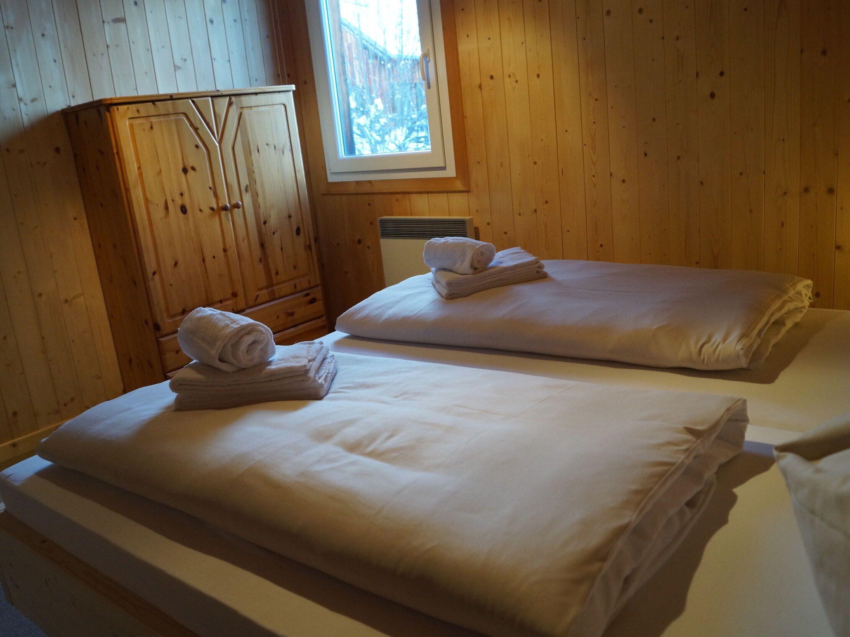 A room with two beds, wooden walls, a window, and a wardrobe.