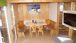 A cozy wooden dining area with a table and chairs, a television, and a window with a view of mountains. - Dreamy Chalet on the Slopes (Sankt Georgen am Kreischberg)