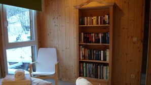 A room with a wooden bookshelf filled with books, a white chair, and a bed with neatly folded towels. - Dreamy Chalet on the Slopes (Sankt Georgen am Kreischberg)