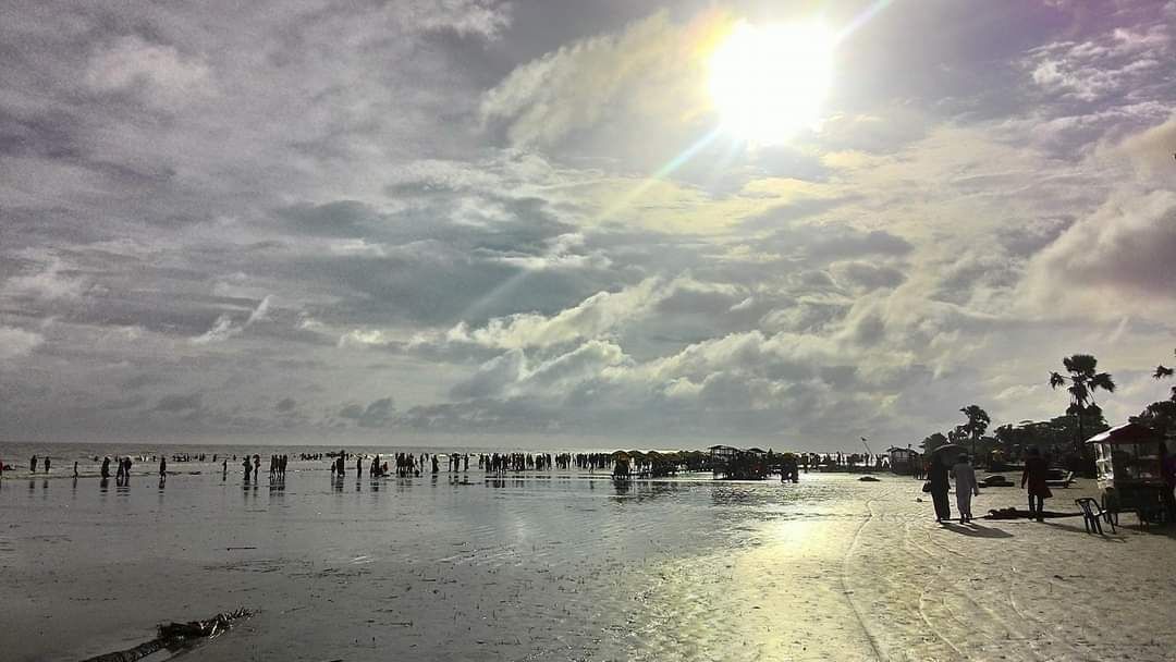 A beach with people and umbrellas, a clear sky, and a sun shining.