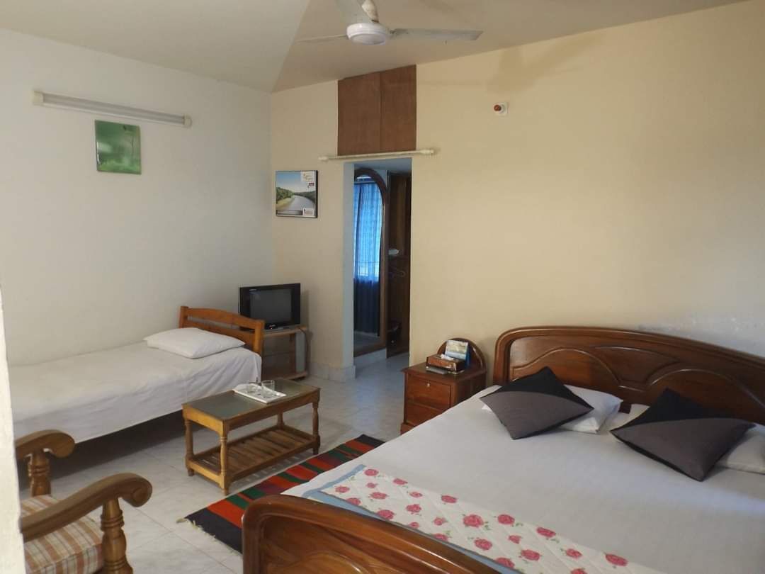 A room with two single beds, a wooden desk, a television, and a ceiling fan.