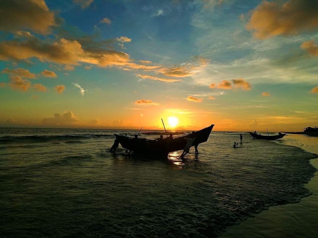 A sunset over a beach with boats and people.