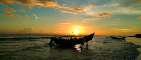 A sunset over a beach with boats and people.