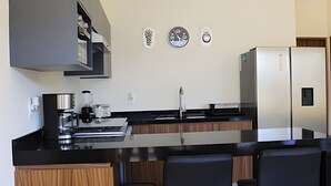 A modern kitchen with a central island, bar stools, a refrigerator, and a coffee machine. - 2BR ·2 Pools ·Ground Floor ·Balcony ·15 min Beach (Mezcales)