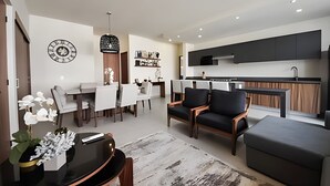 A modern living room with a dining area, a kitchen, and a seating area with a coffee table and chairs. - 2BR ·2 Pools ·Ground Floor ·Balcony ·15 min Beach (Mezcales)