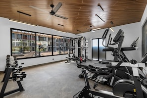 A gym with various exercise equipment, large windows, and a wooden ceiling.