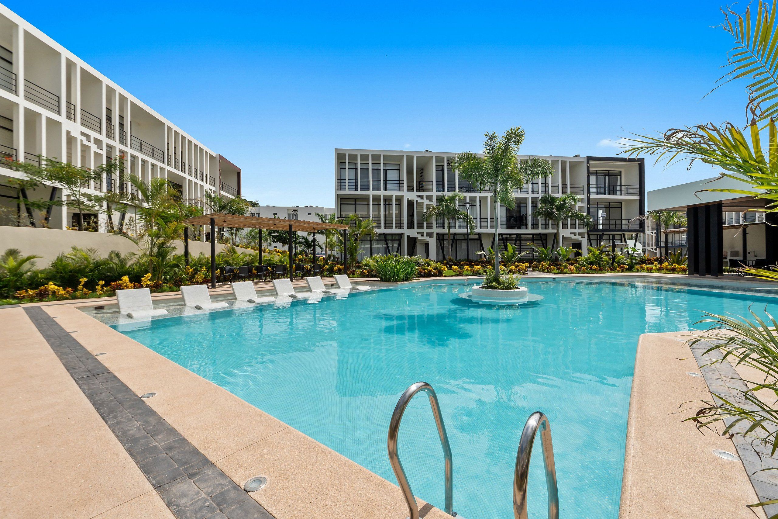 A swimming pool with lounge chairs, a palm tree, and a modern building in the background.