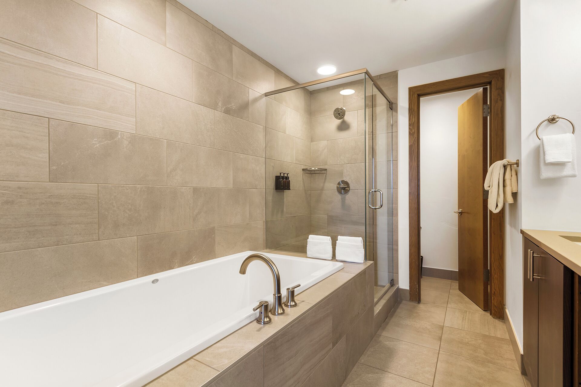 A modern bathroom with a large bathtub, a glass-enclosed shower, and a wooden vanity.