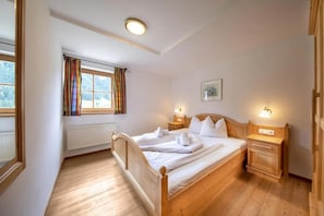 A bedroom with a wooden bed, a window with curtains, a bedside table with a lamp, and a wall-mounted picture. - Alpine Chalet in Wald im Pinzgau for 12 (Wald im Pinzgau)