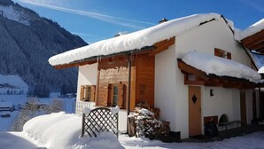 A snow-covered chalet with a wooden facade, a balcony, and a mountain backdrop. - Alpine Chalet in Wald im Pinzgau for 12 (Wald im Pinzgau)