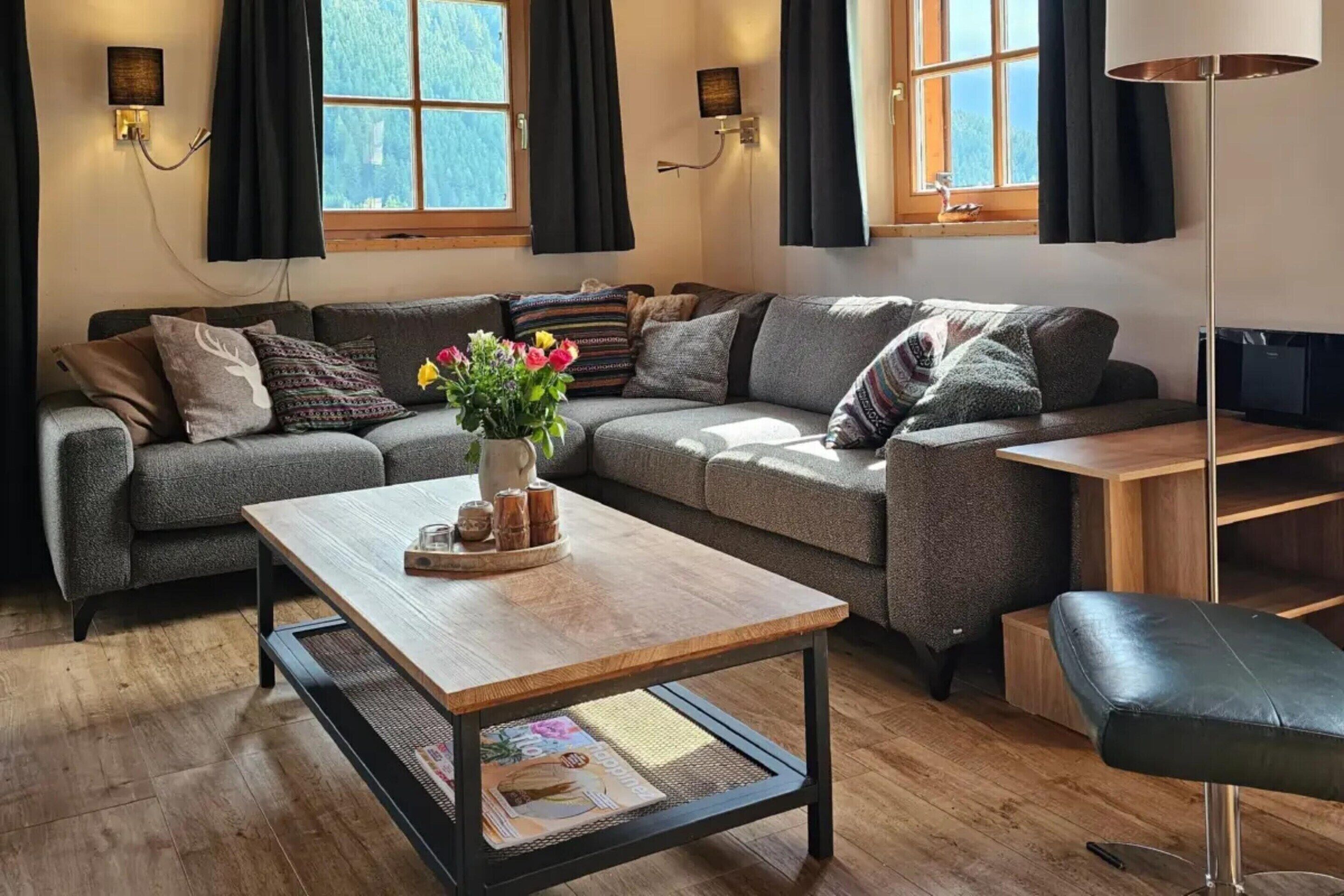 Una sala de estar moderna con un sofá gris, una mesa de centro de madera y un reposapiés de cuero negro.
