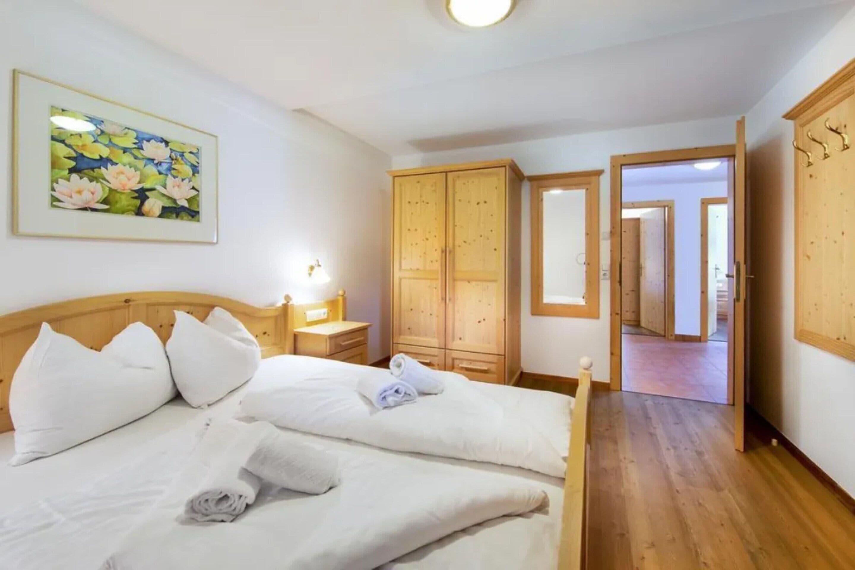 A hotel room with a bed, a nightstand, a lamp, a wooden wardrobe, and a painting of flowers.
