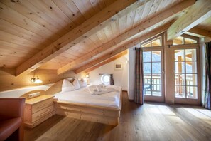 A wooden room with a sloped ceiling, a bed with white linens, a bedside table, a chair, and a window with curtains. - Alpine Chalet in Wald im Pinzgau for 12 (Wald im Pinzgau)