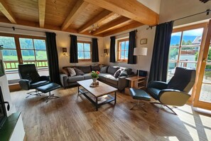 A spacious living room with a wooden ceiling, a sofa set, a coffee table, and large windows offering a view of the outdoors. - Alpine Chalet in Wald im Pinzgau for 12 (Wald im Pinzgau)