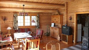 L’intérieur chaleureux d’un chalet en bois comprend un coin repas, des meubles en bois, un téléviseur et un poêle d’époque.