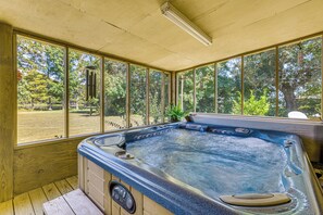 Un jacuzzi con cubierta de madera y amplios ventanales que ofrecen vistas a un área boscosa.