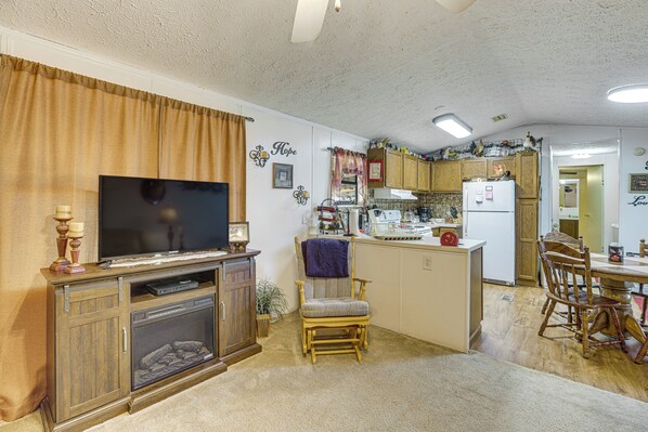 Una sala de estar con televisor, chimenea, comedor con mesa y sillas, y cocina con armarios y electrodomésticos.