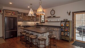 Una cocina con una isla central, taburetes de bar, un refrigerador y luces colgantes.