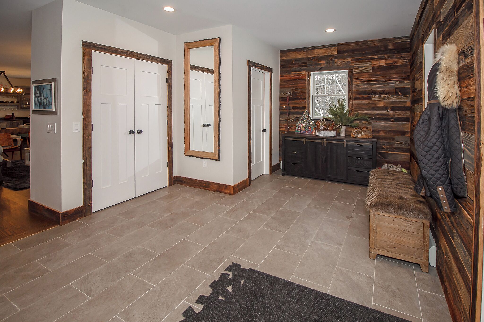 A spacious hallway with a wooden accent wall, a bench, and a large mirror.